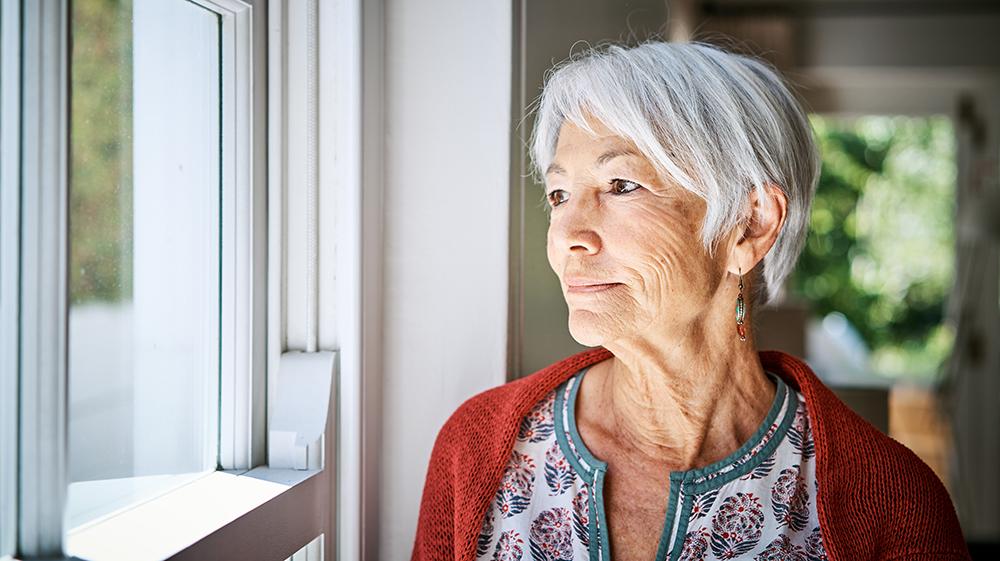 Older woman in a red cardigan gazing out a window